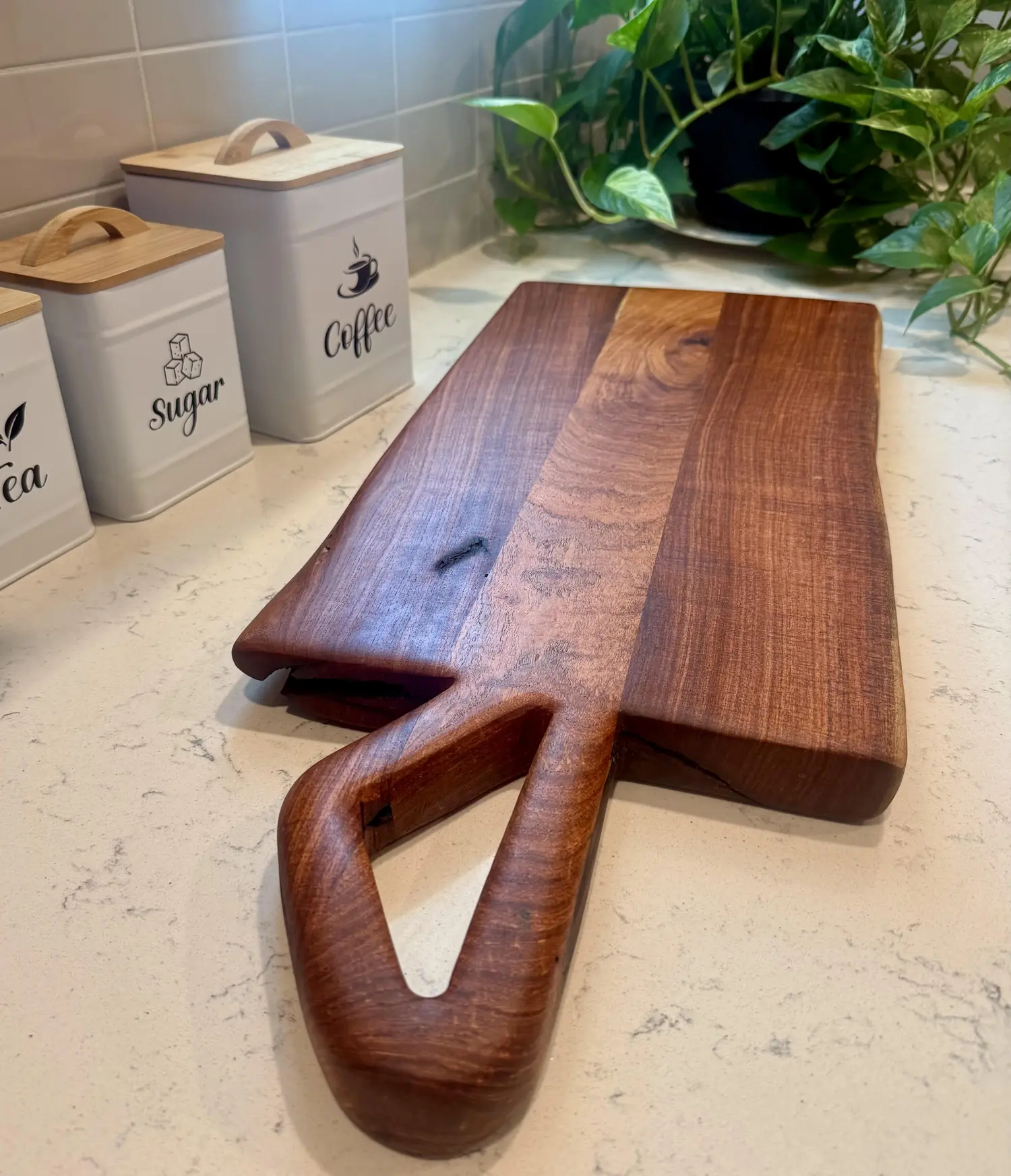 Handmade wood cutting board with a sculpted open handle on a kitchen counter